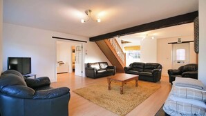 A spacious living room with a wooden floor, a black leather sofa, a wooden coffee table, and a staircase leading to an upper level.
