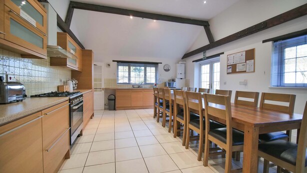A kitchen with wooden cabinets, a stove, and a dining area with wooden chairs and a table.