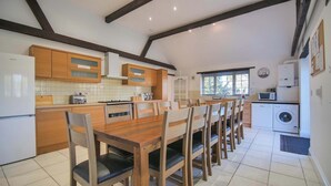 A kitchen with wooden cabinets, a dining table with chairs, a washing machine, and a clock on the wall.