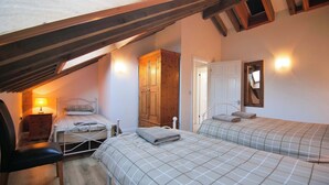 A bedroom with two beds, a wooden wardrobe, a desk with a lamp, and a mirror on the wall.