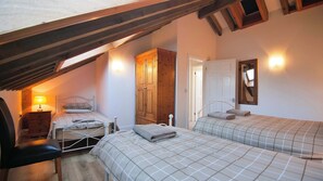 A bedroom with two beds, a wooden wardrobe, a desk with a lamp, and a mirror on the wall.