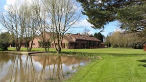 A building with a pond in front, surrounded by trees and a grassy area.
