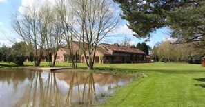 A building with a pond in front, surrounded by trees and a grassy area.