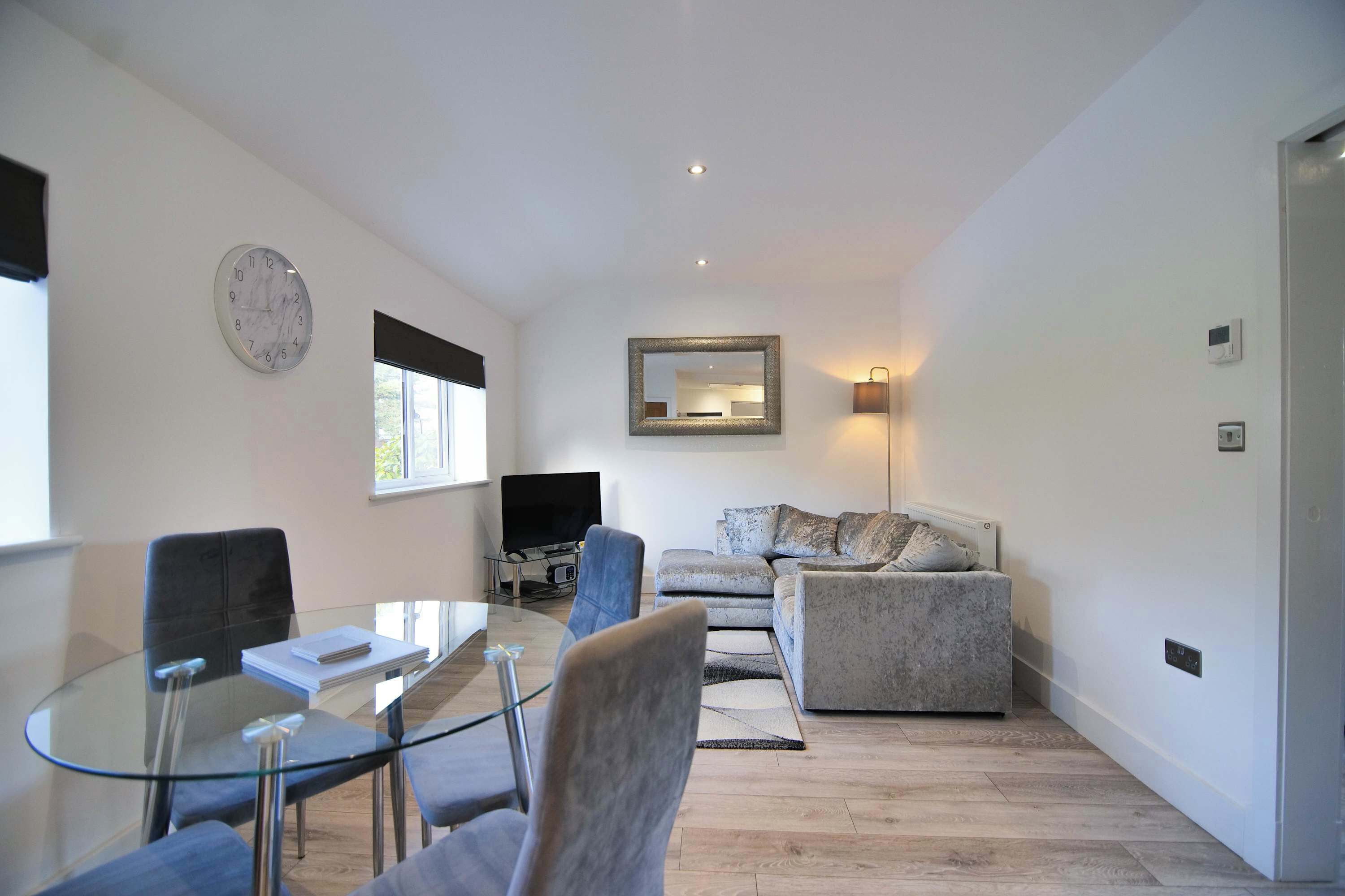 A modern living room with a glass table, chairs, a sofa, a TV, and a clock on the wall.