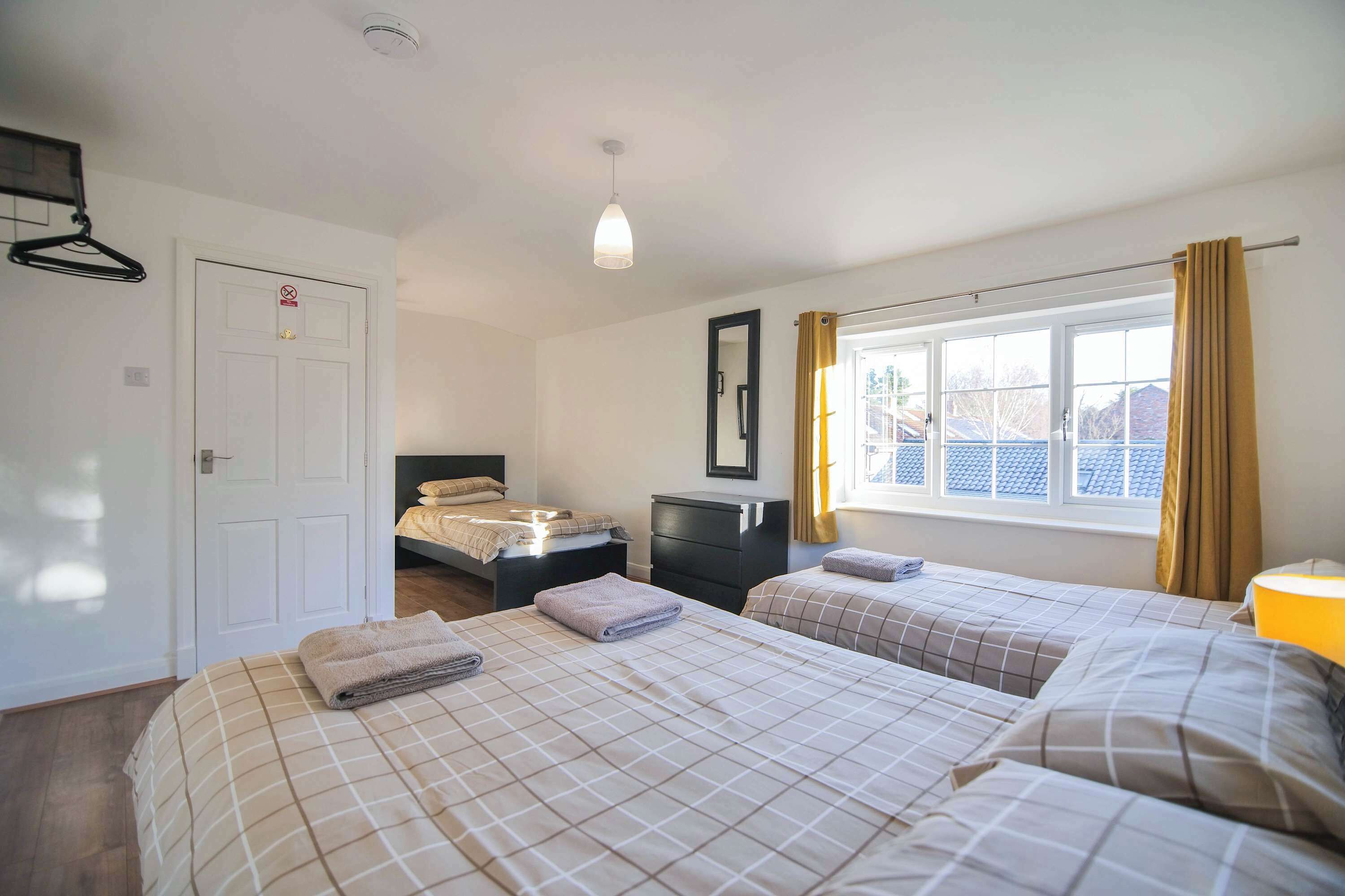 A hotel room with two beds, a dresser, a mirror, a window with curtains, and a hanging light fixture.