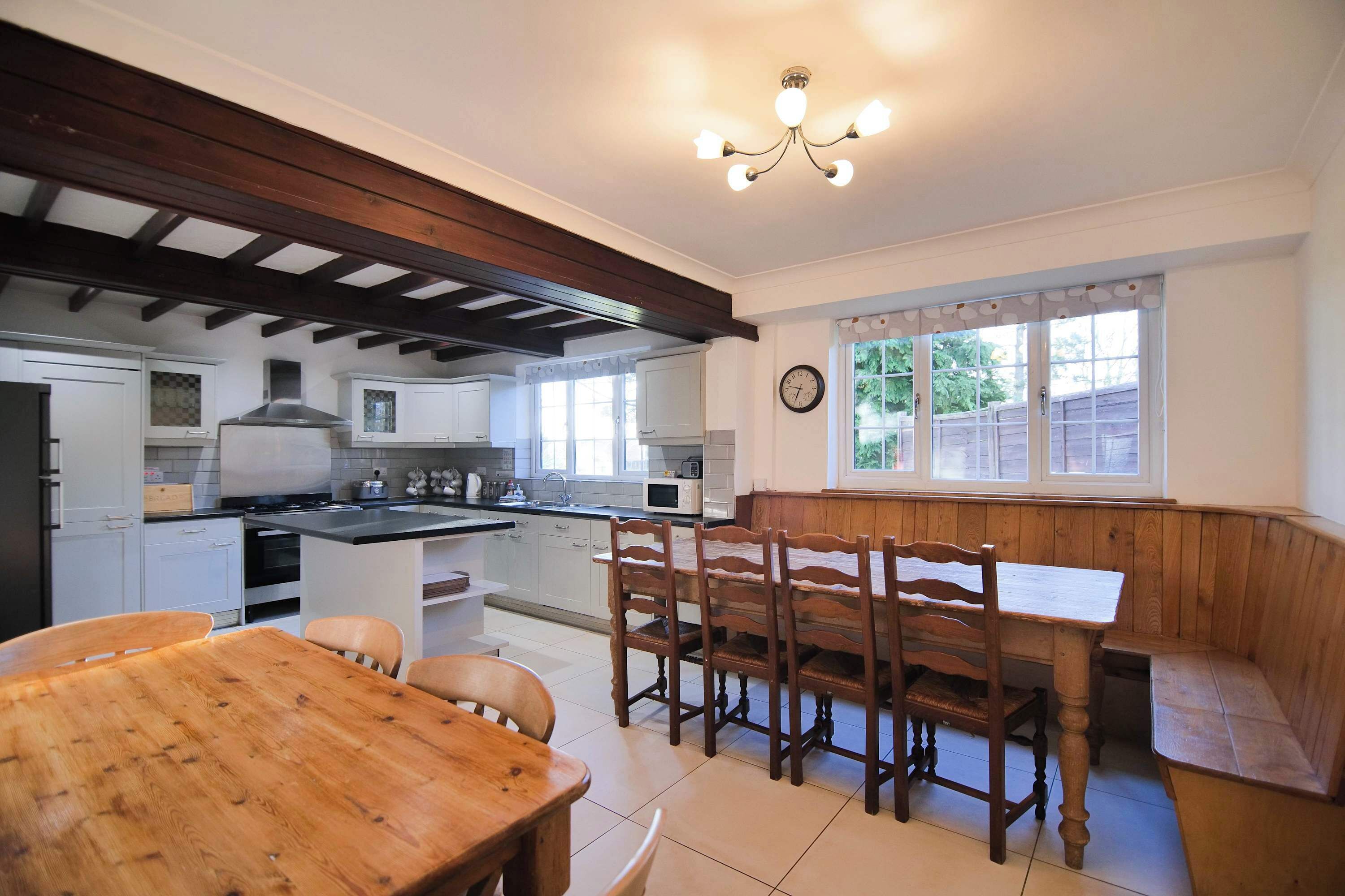 A kitchen with a wooden table and chairs, a clock on the wall, and a window with a view of greenery.