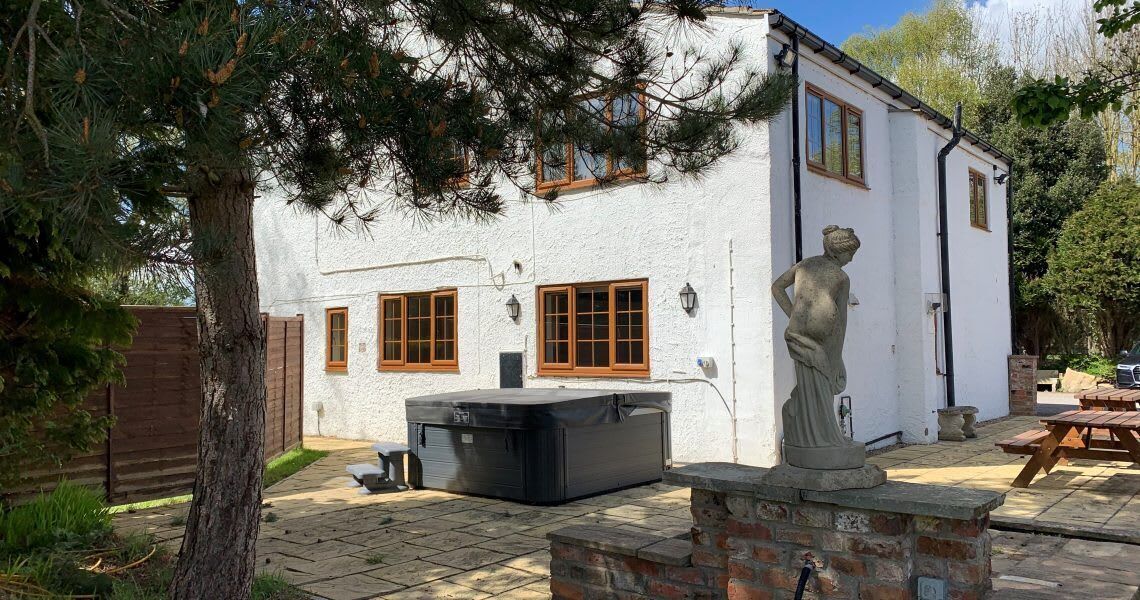 A white building with wooden windows, a statue, and a hot tub in the yard.