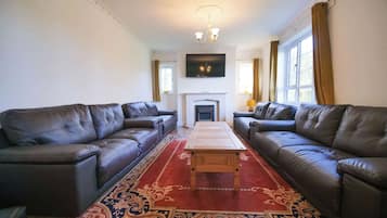 A living room with two leather sofas, a wooden coffee table, a red patterned rug, a fireplace, and a television mounted on the wall.