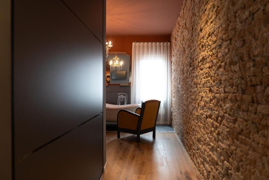 Ein Zimmer mit Steinwand, Holzboden, einem Sessel, einem Bett und einer Chandelüster.