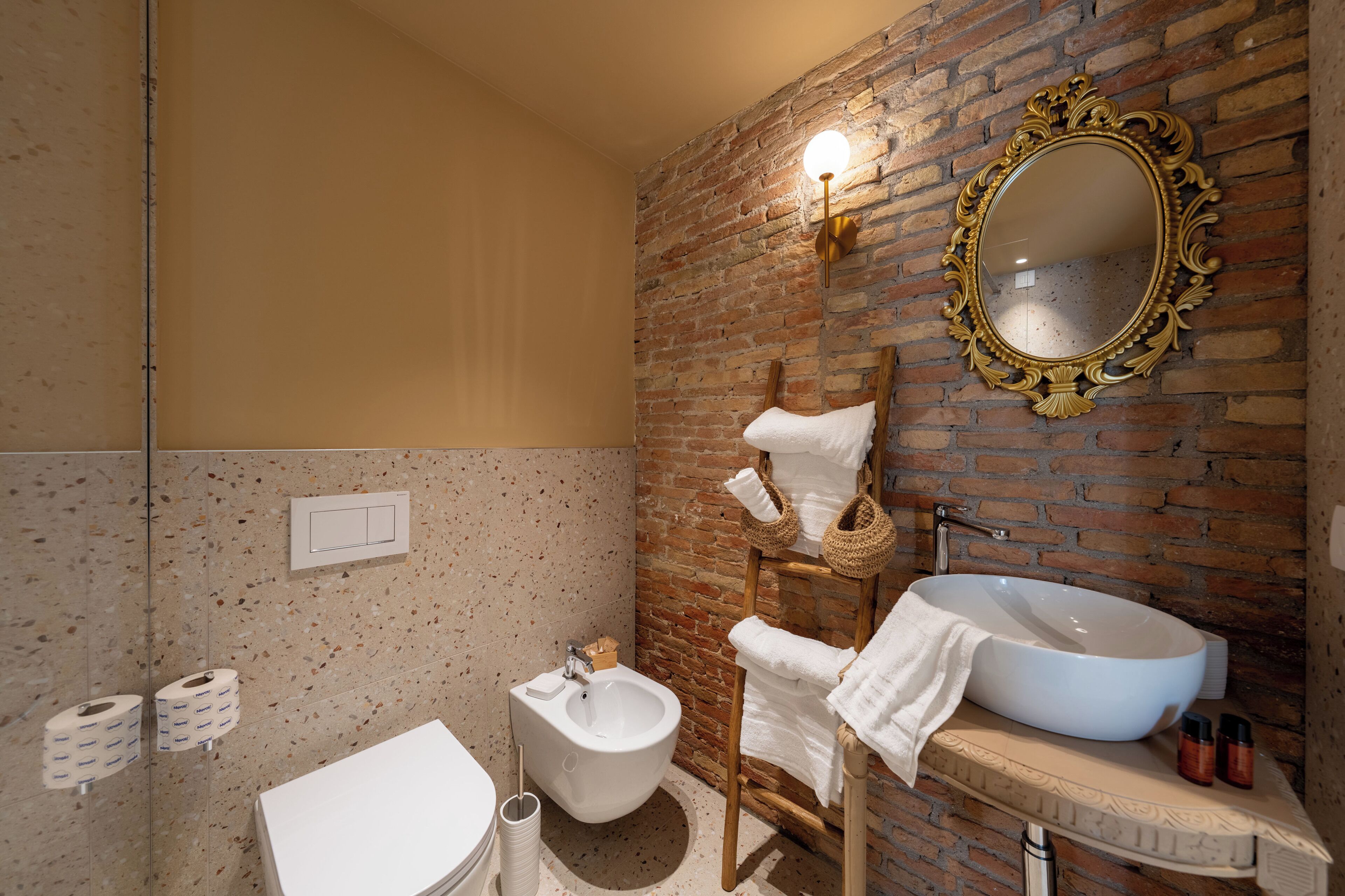 Une salle de bain avec un lavabo blanc, un bidet, un miroir doté d’un cadre orné et un porte-serviettes.