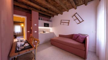 A compact living space with a kitchenette, a dining area with a table and chairs, and a sofa with cushions.