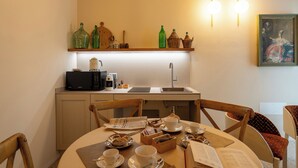 A dining area with a table set for two, a microwave, a coffee maker, and a shelf above the counter with decorative items. - Spaccavento Boutique Rooms (Chioggia)
