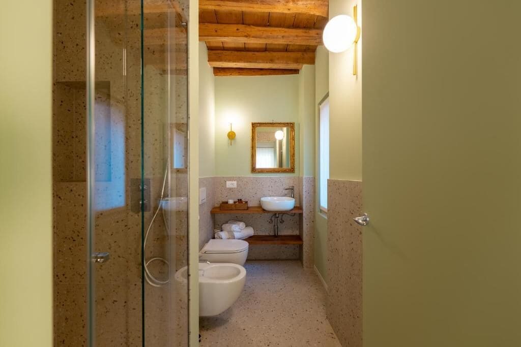 Un baño con cabina de ducha de vidrio, un lavamanos, inodoro y un espejo en la pared.