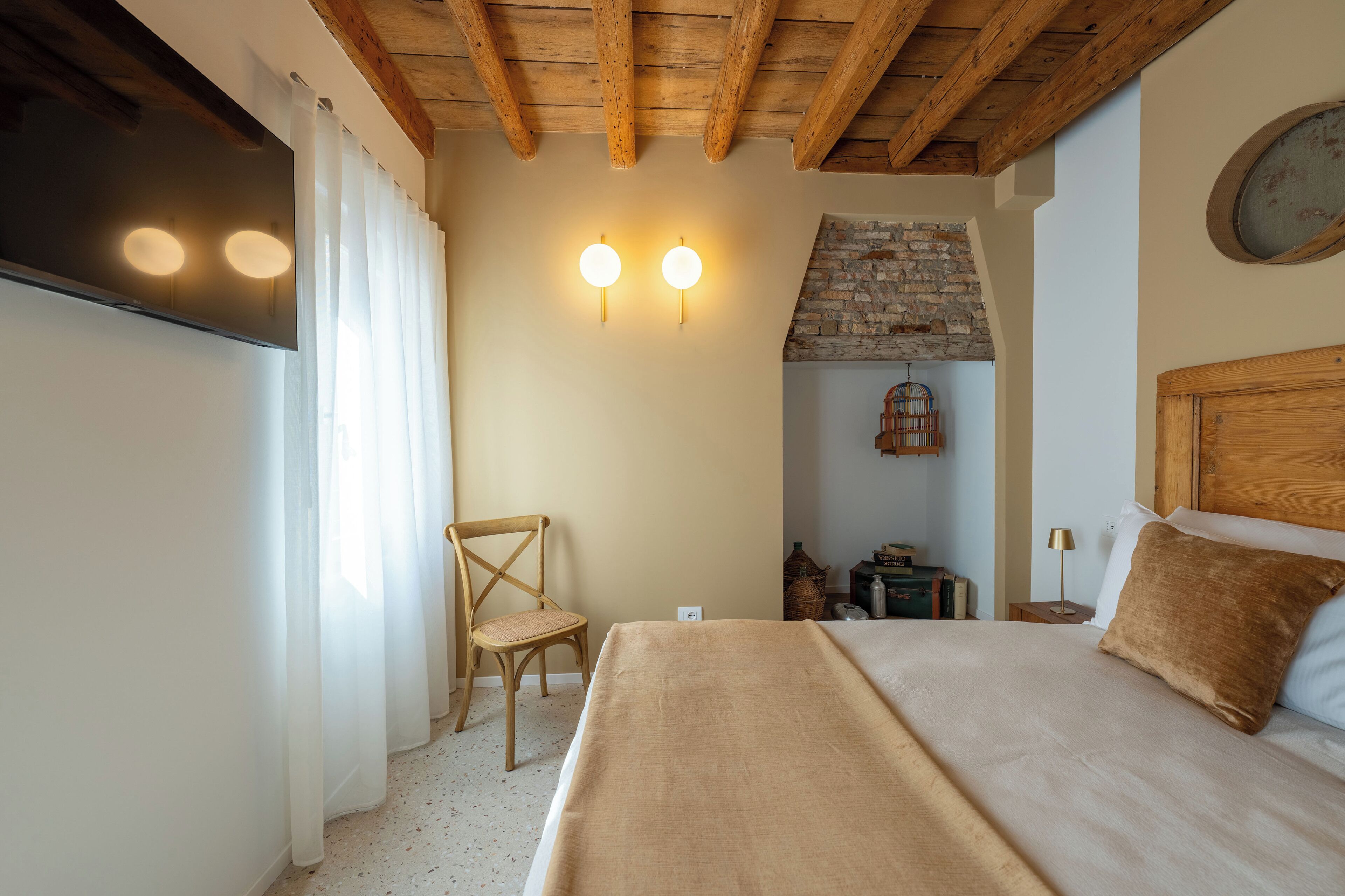 Een slaapkamer met een bed, een stoel, een houten plafond, een wandklok en een open haard van baksteen.