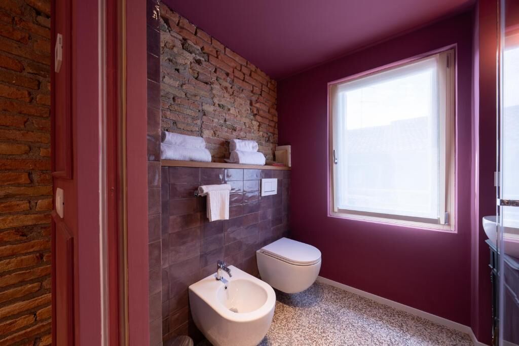 Een badkamer met een bakstenen muur, een bidet, toilet en een raam dat voor natuurlijk licht zorgt.