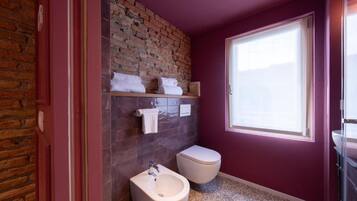 Een badkamer met een bakstenen muur, een bidet, toilet en een raam dat voor natuurlijk licht zorgt.