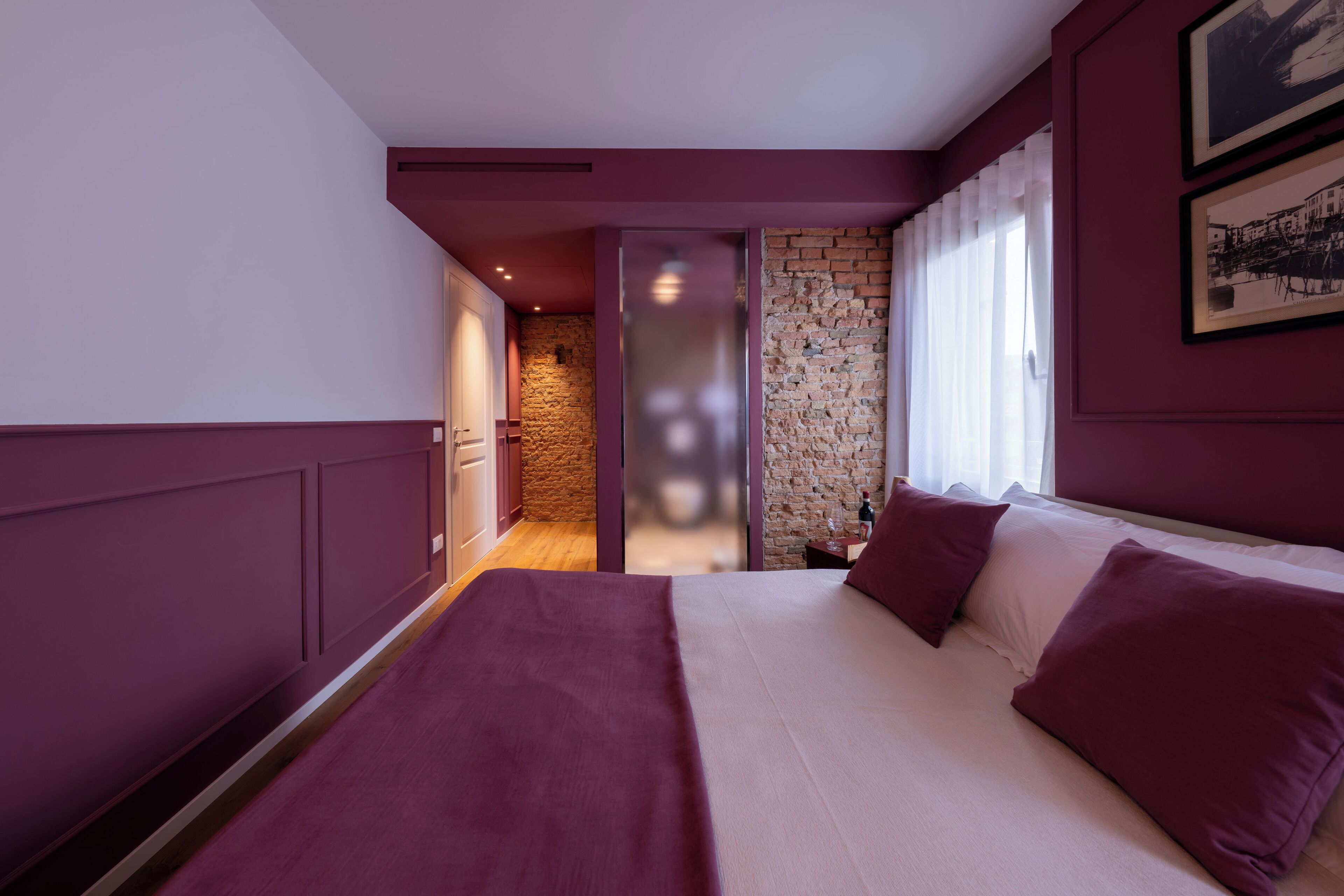 A bedroom with a large bed, a brick wall, and a window with curtains.