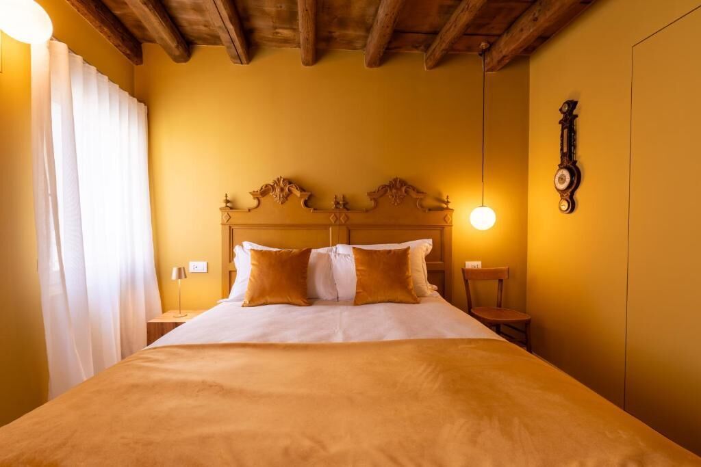 A hotel room with a wooden headboard, a bed with white and brown bedding, a bedside table with a lamp, and a wall clock.