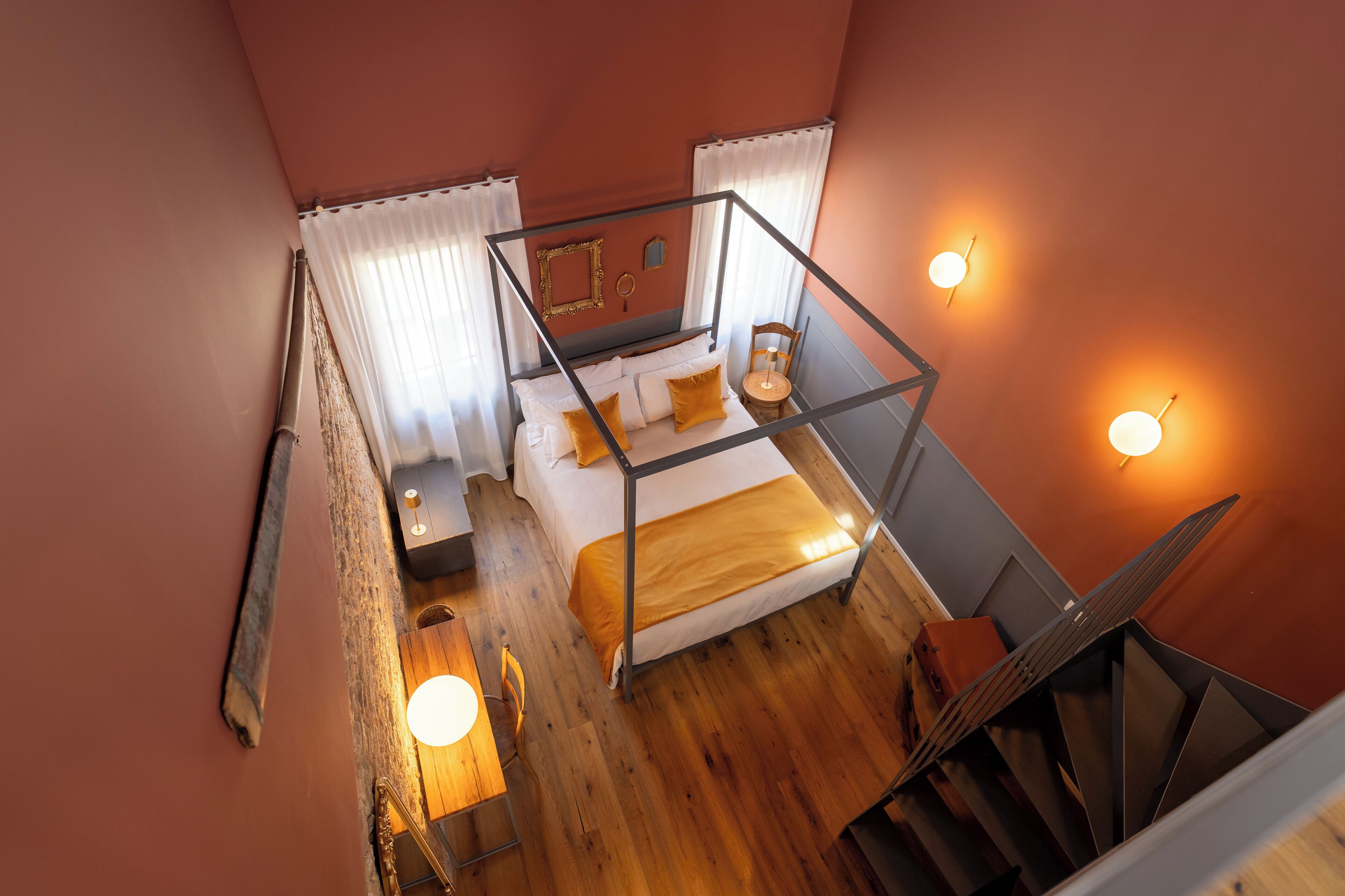 Een slaapkamer met een bed, nachtkastje, lamp en uitzicht op de trap.