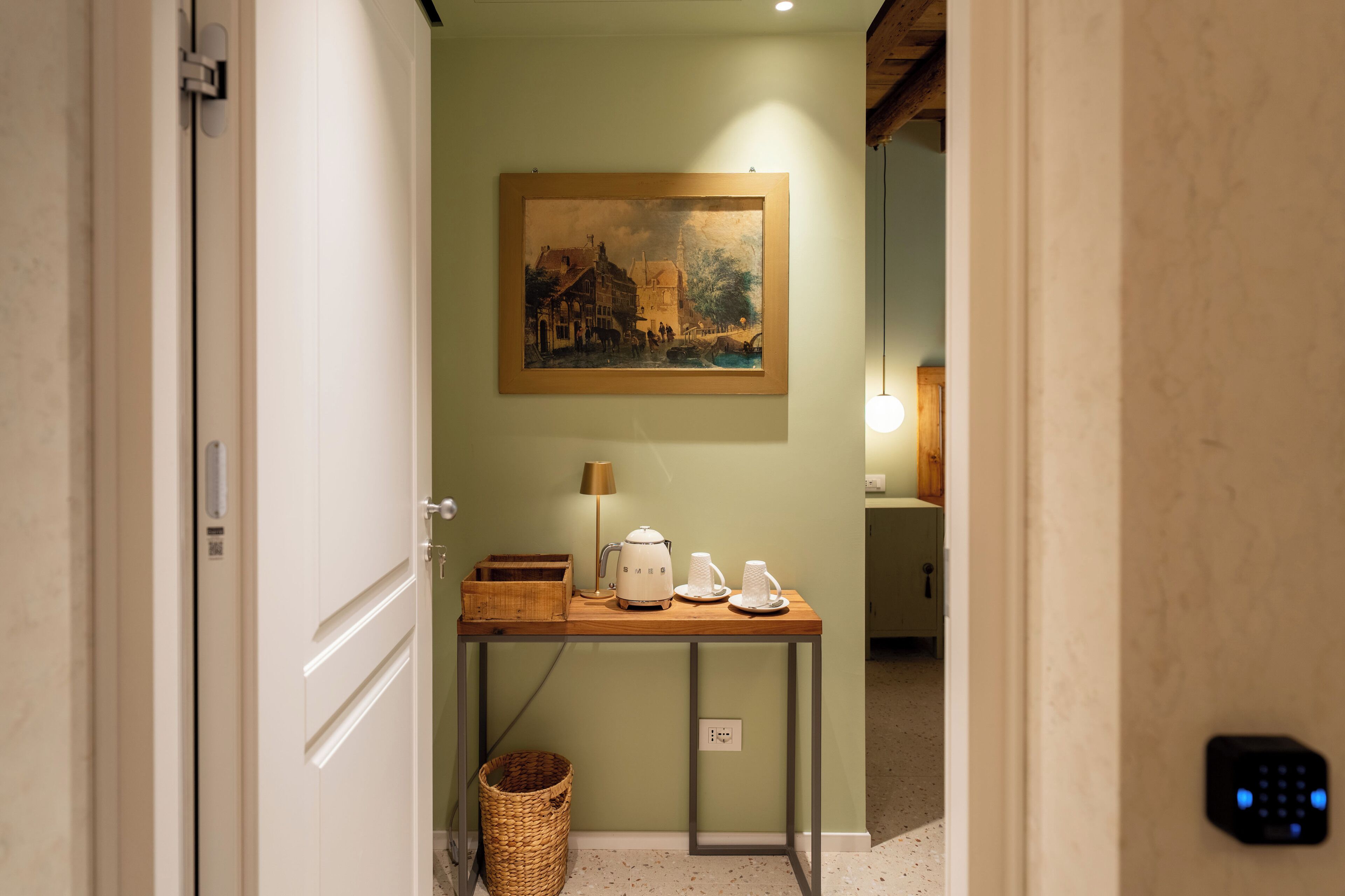 A hallway with a painting, a table with a kettle and cups, and a basket.