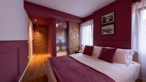 A bedroom with a large bed, a stone wall, and a door leading to another room. - Spaccavento Boutique Rooms (Chioggia)
