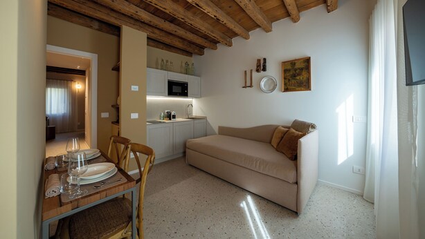 A compact living space with a kitchenette, a dining area with a table set for two, a sofa, and a television. - Spaccavento Boutique Rooms (Chioggia)