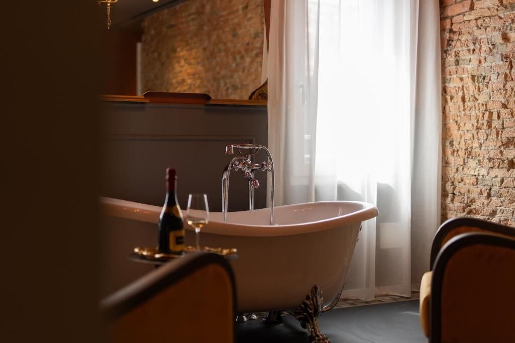 Un baño con una bañera independiente, una botella de vino y una copa sobre el mostrador.