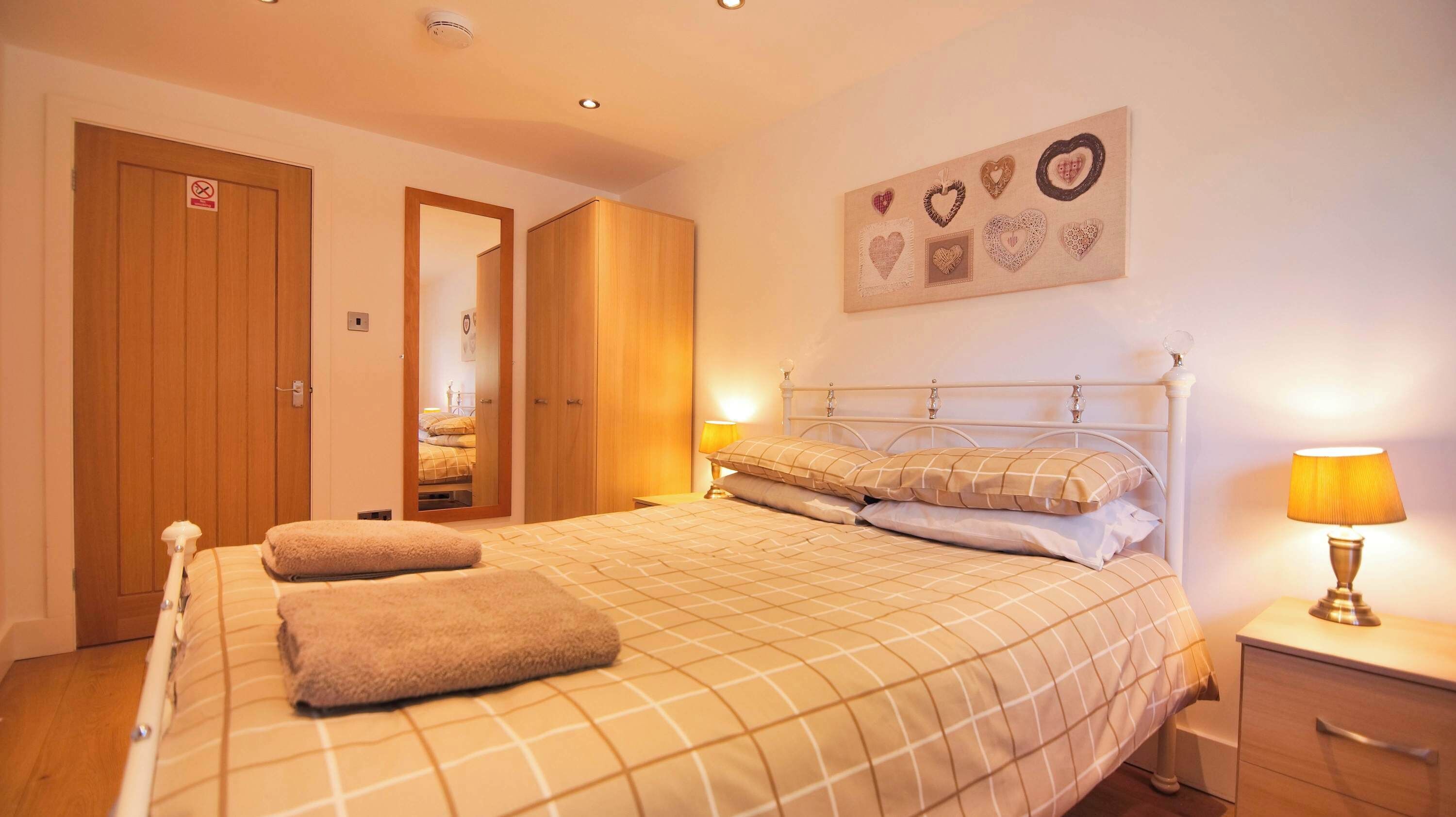 A bedroom with a bed, two bedside tables, a nightstand, a mirror, and a wall with heart-shaped decorations.