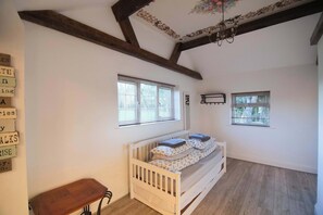 Una habitación con una cuna de madera, dos ventanas y un banco de madera.