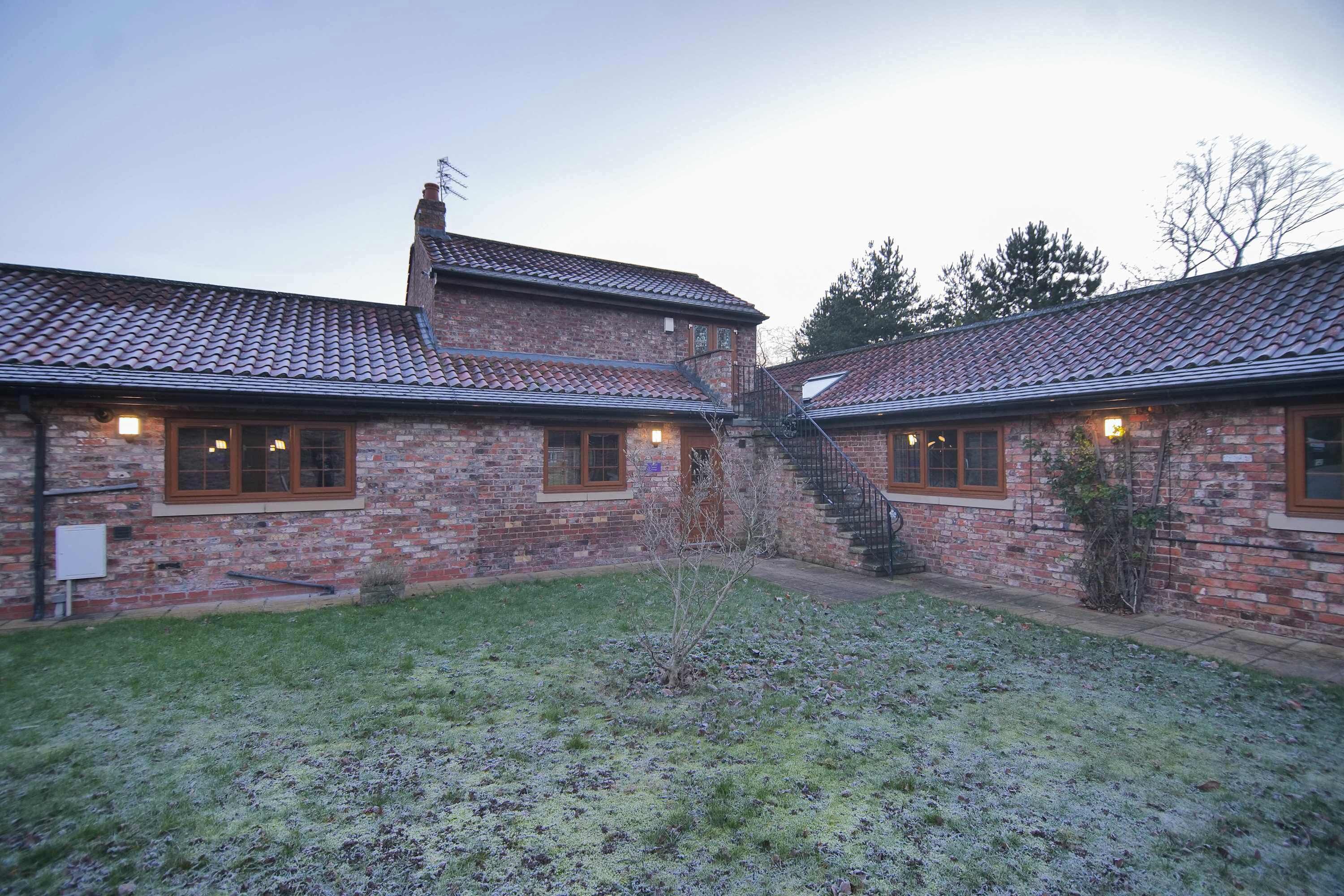 A brick building with a tiled roof, a small garden, and a staircase leading to an upper level.