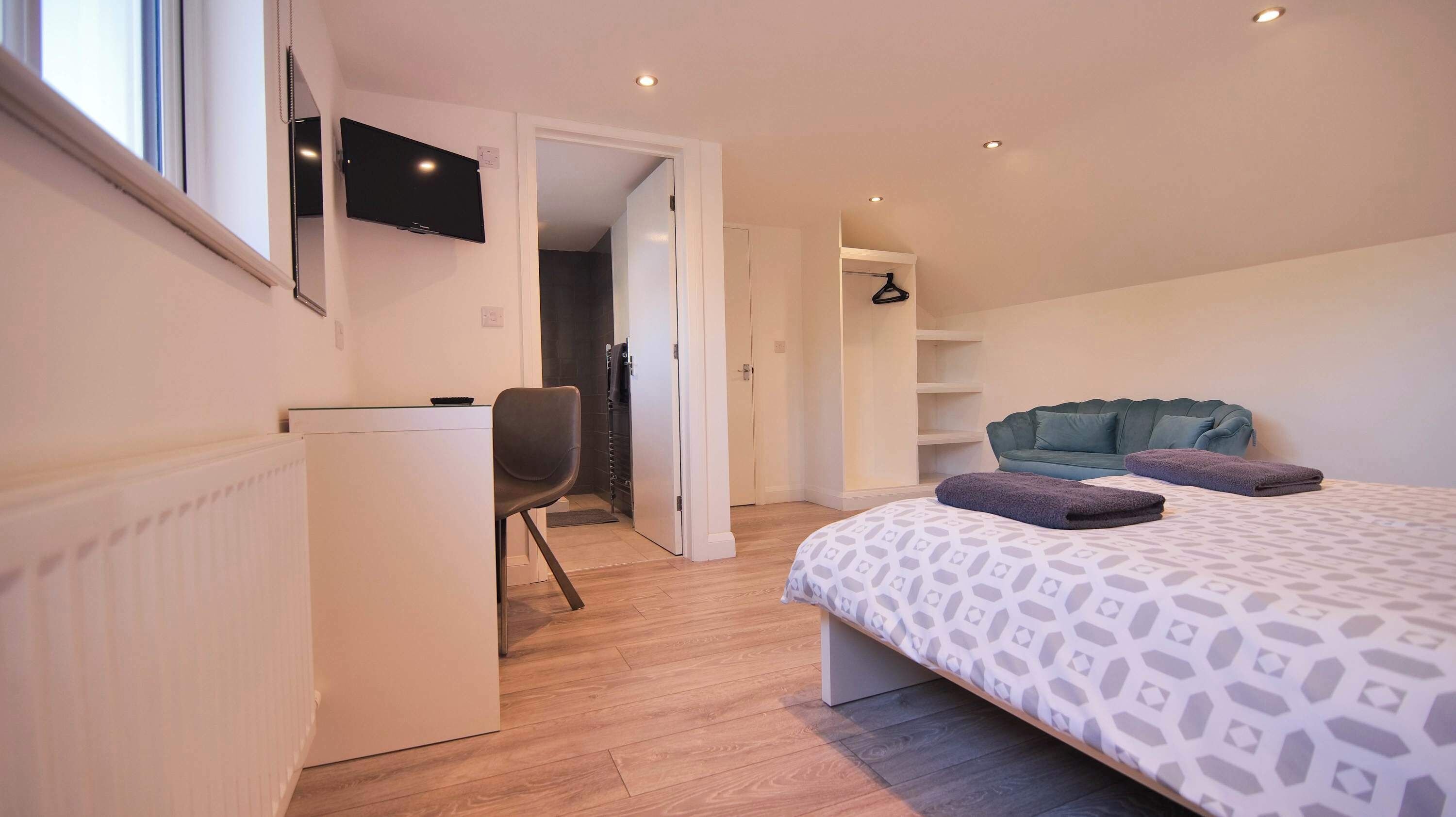 A bedroom with a bed, a desk, a chair, a TV, and a wardrobe.