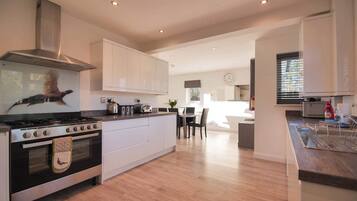 A modern kitchen with a gas stove, oven, and stainless steel range hood. There is a dining area with a table and chairs, and a large window providing natural light.