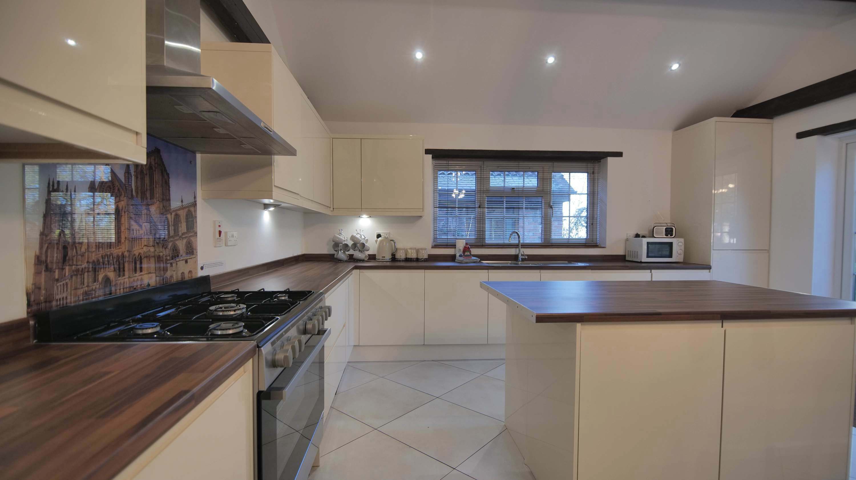 A modern kitchen with a gas stove, white cabinets, a window with blinds, and a microwave.