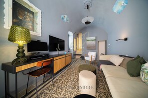 Ein modernes Wohnzimmer mit Fernseher, Holzschreibtisch, gemustertem Teppich, Sofa und einer dekorativen Lampe.