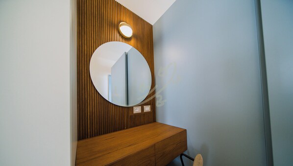 Ein Badezimmer mit einem Holzkosmetikschrank, einem runden Spiegel und einer Wandleuchte.