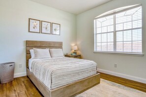 A bedroom with a bed, a nightstand, a lamp, a window, and three framed pictures on the wall. - Pink Apple l Modern Comfort (Davenport)