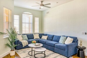 A living room with a blue sectional sofa, a round coffee table, and a potted plant. - Pink Apple l Modern Comfort (Davenport)