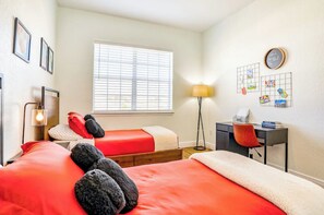 A bedroom with two beds, a desk, a lamp, and a window with blinds. - Pink Apple l Modern Comfort (Davenport)