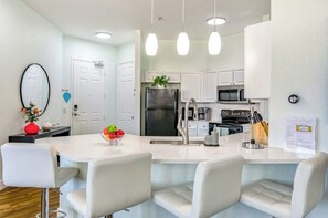 Een moderne keuken met witte kasten, een centraal eiland met zitplaatsen, roestvrijstalen apparatuur en hanglampen.