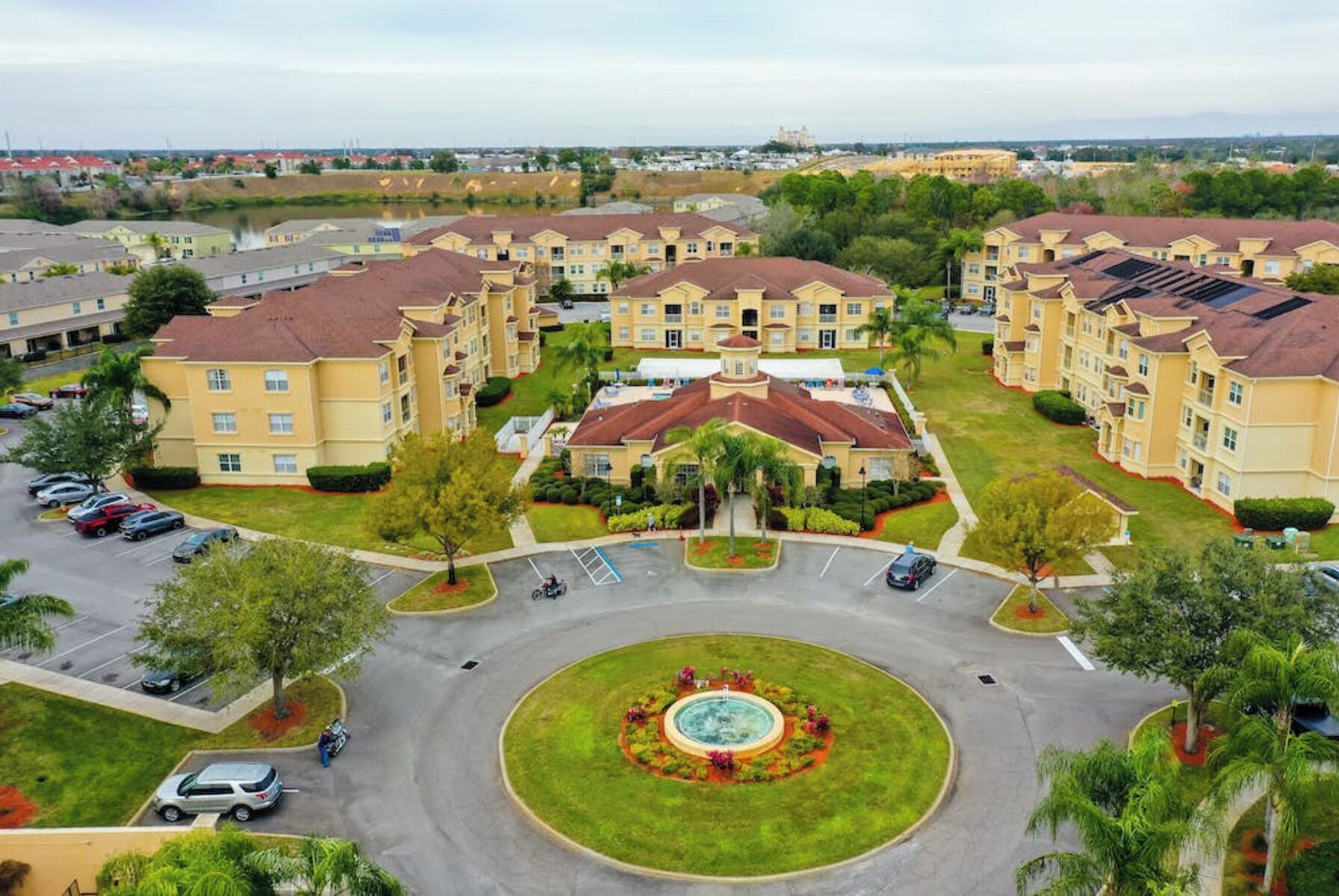 A residential complex with multiple apartment buildings, a central courtyard with a fountain, and a parking area.