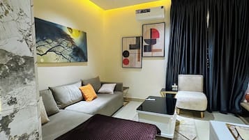A modern bedroom with a bed, sofa, armchair, and a painting on the wall.
