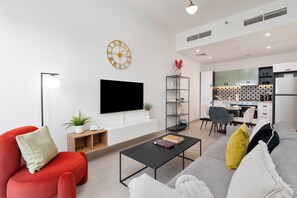 Uma sala de estar moderna com televisão de tela plana, um sofá vermelho, um sofá cinza, uma mesa de centro e uma estante.