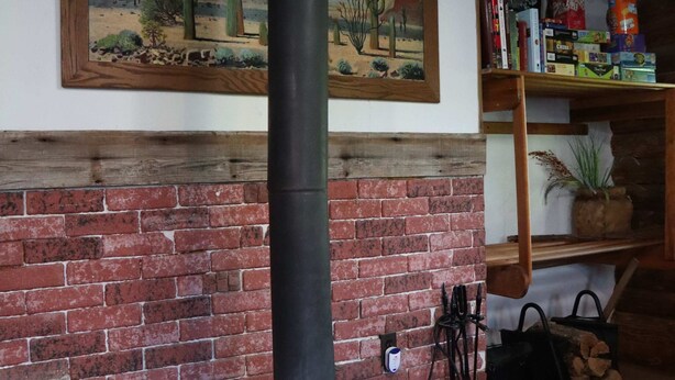 Un camino in mattoni con canna fumaria nera, un quadro sopra e una libreria con diversi oggetti.