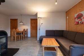 A living room with a wooden floor, a sofa, a dining table with chairs, a lamp, and a painting on the wall. - Familienfreundlicher Doppelbungalow mit Terrasse im Ferienpark Mirow (Mirow)