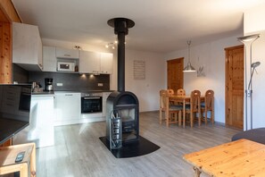 A modern kitchen with a wood-burning stove, a dining area with a wooden table and chairs, and a compact living space. - Familienfreundlicher Doppelbungalow mit Terrasse im Ferienpark Mirow (Mirow)