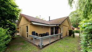 A wooden cabin with a tiled roof, a deck, and a patio area with outdoor furniture. - Familienfreundlicher Doppelbungalow mit Terrasse im Ferienpark Mirow (Mirow)