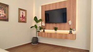Una habitación moderna con televisor montado, panel de madera en la pared, plantas en macetas y un estante pequeño.