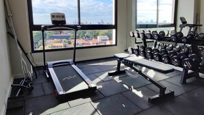 Un gimnasio con cinta de correr, banco y estante para pesas.