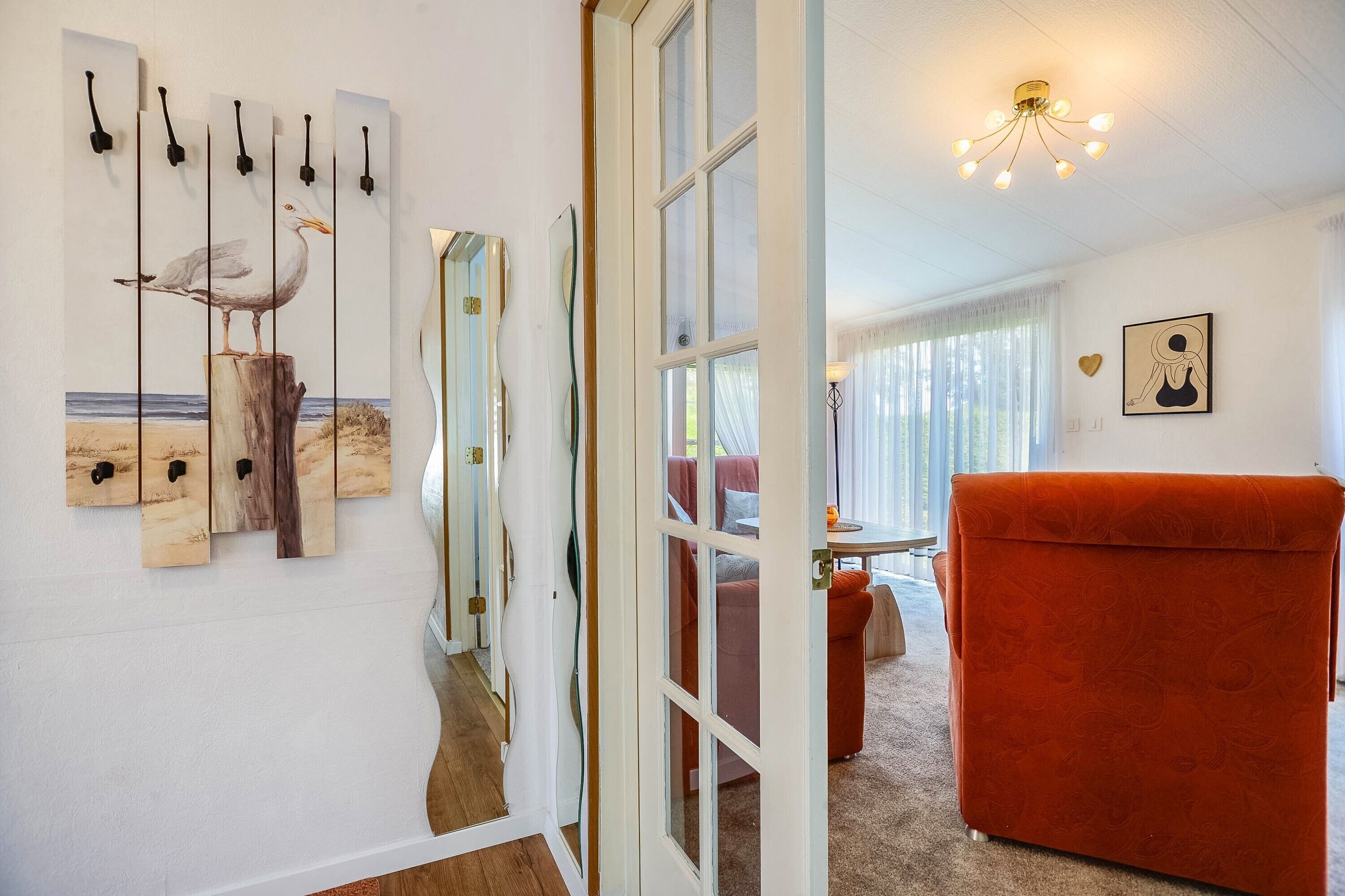 Una habitació amb una cadira vermella, un sòl de fusta, una paret amb obres d'art i una porta que dona a una altra habitació.