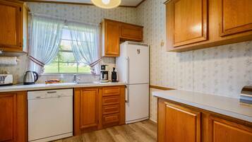 Une cuisine avec des meubles en bois, un réfrigérateur, un lave-vaisselle et une fenêtre avec des rideaux.
